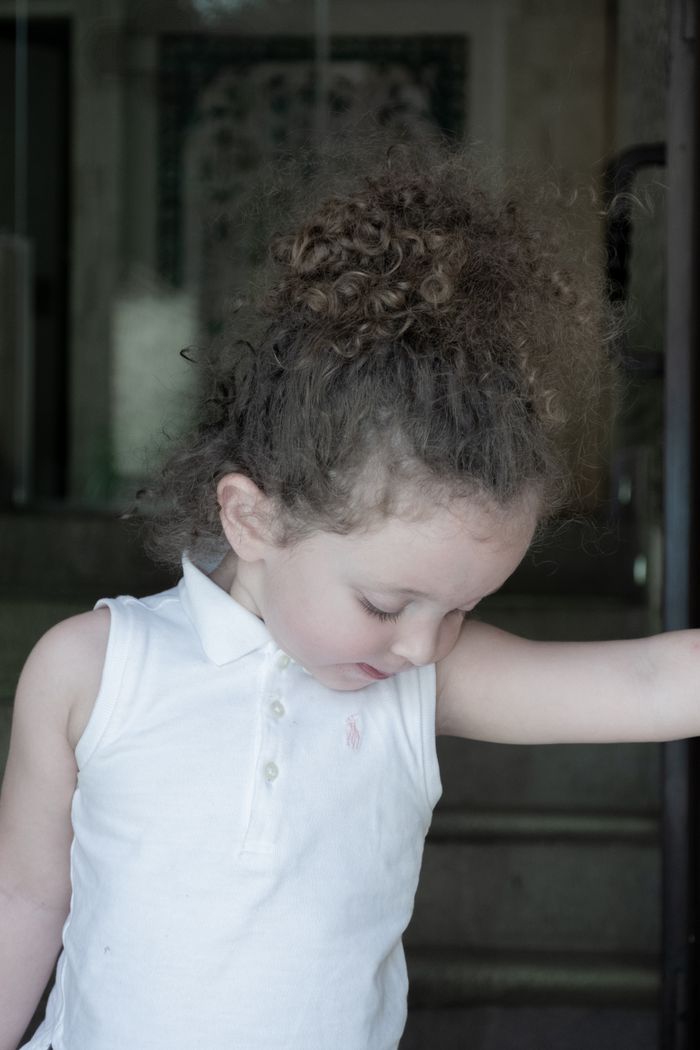 Charming young girl with curly hair looking down, dressed in white, in Isfahan.