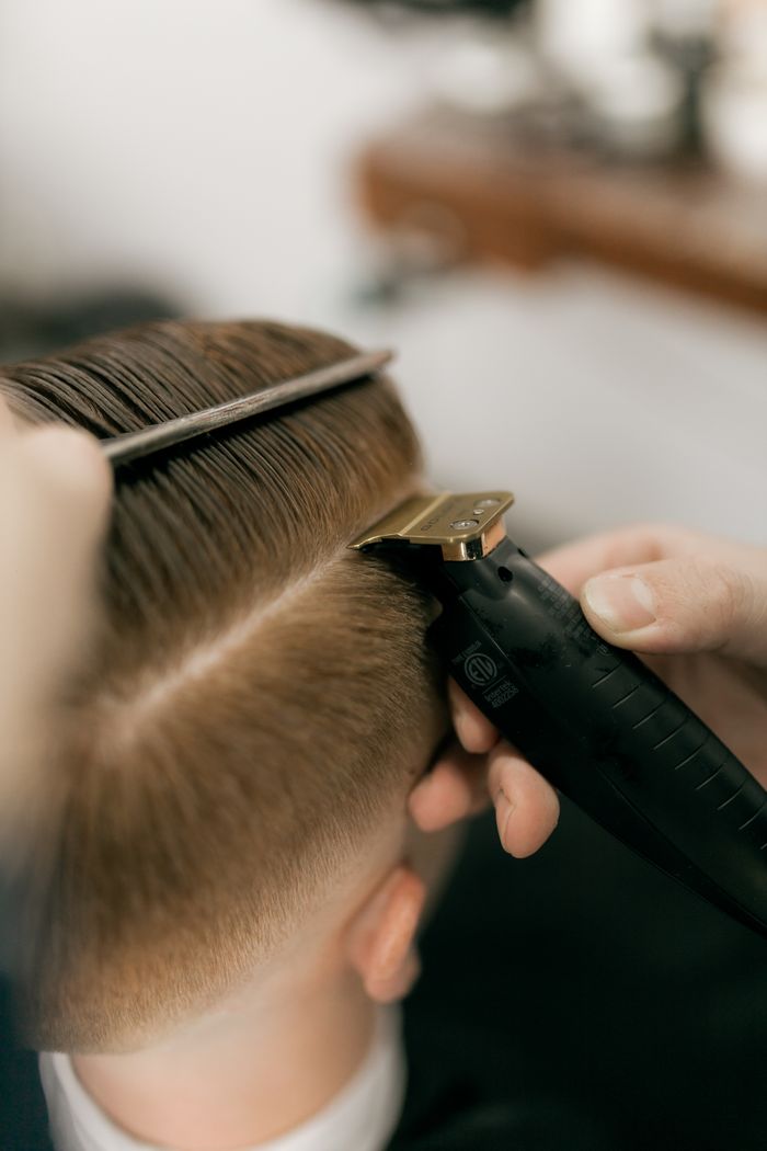 Close-up of a barber using clippers and comb to trim a client's hair at a salon.
