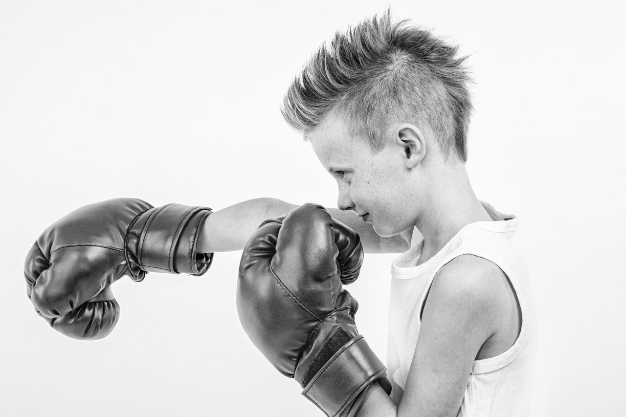 A young boy practicing boxing in a black and white image, wearing gloves and a tank top.