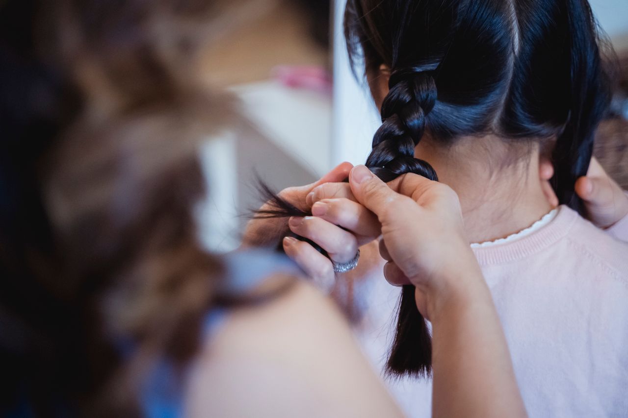 A close-up of hands skillfully braiding a young girl's hair in an indoor setting.