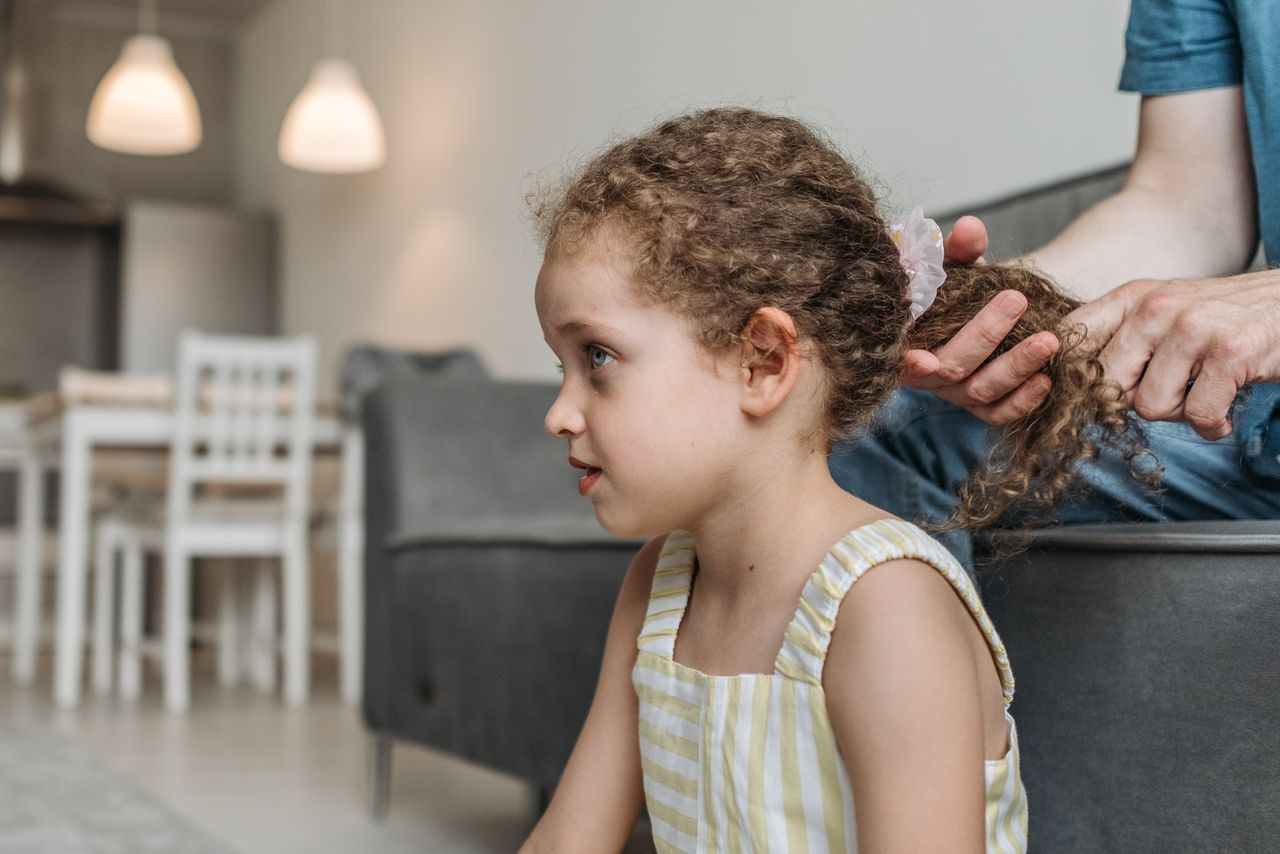 A young girl with curly hair having her hair styled in a cozy home setting.