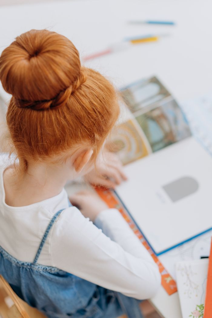 Young girl reading in a classroom environment, focused on a picture book.
