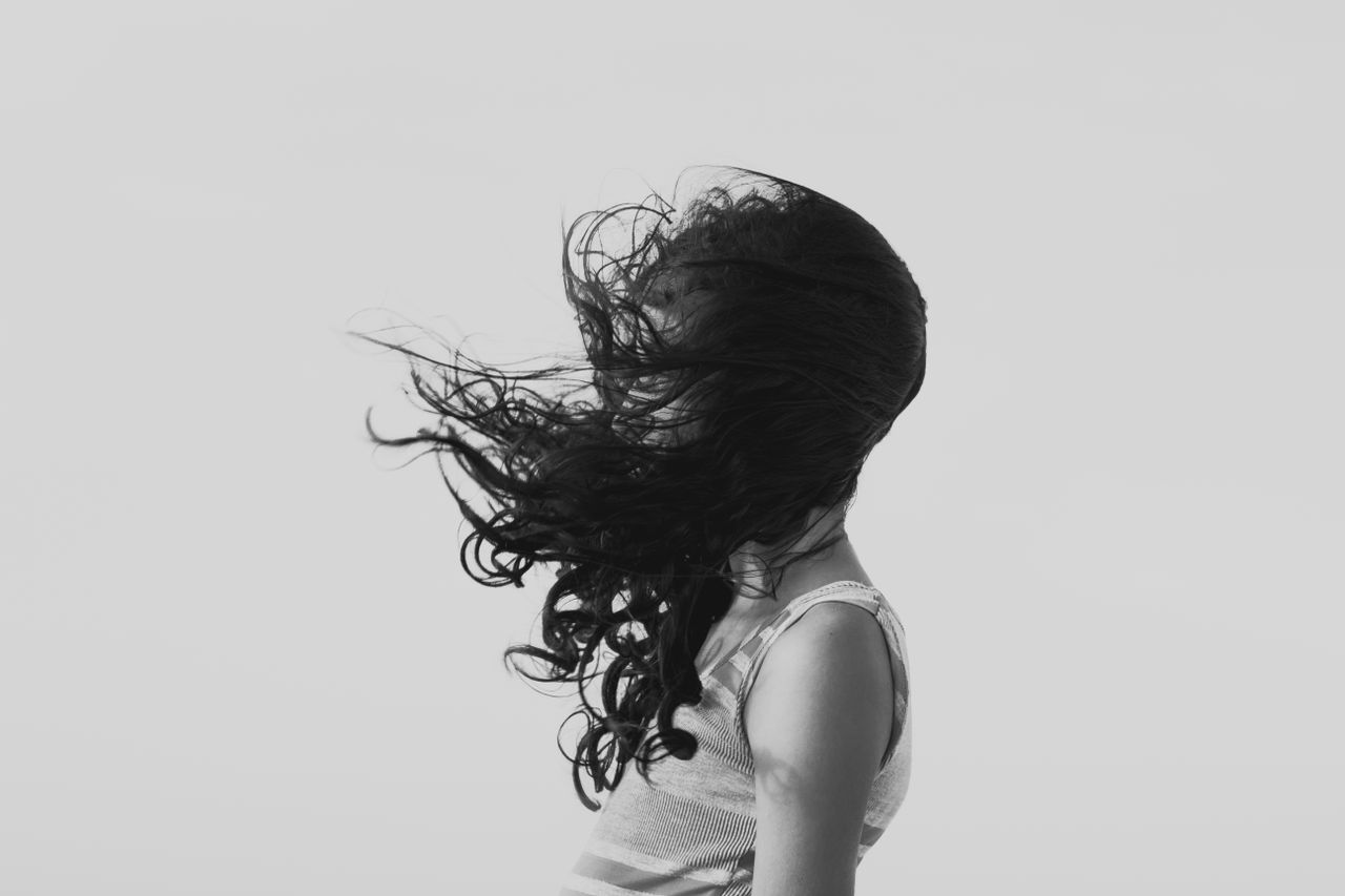 Artistic black and white portrait of a woman with hair covering her face in the wind.